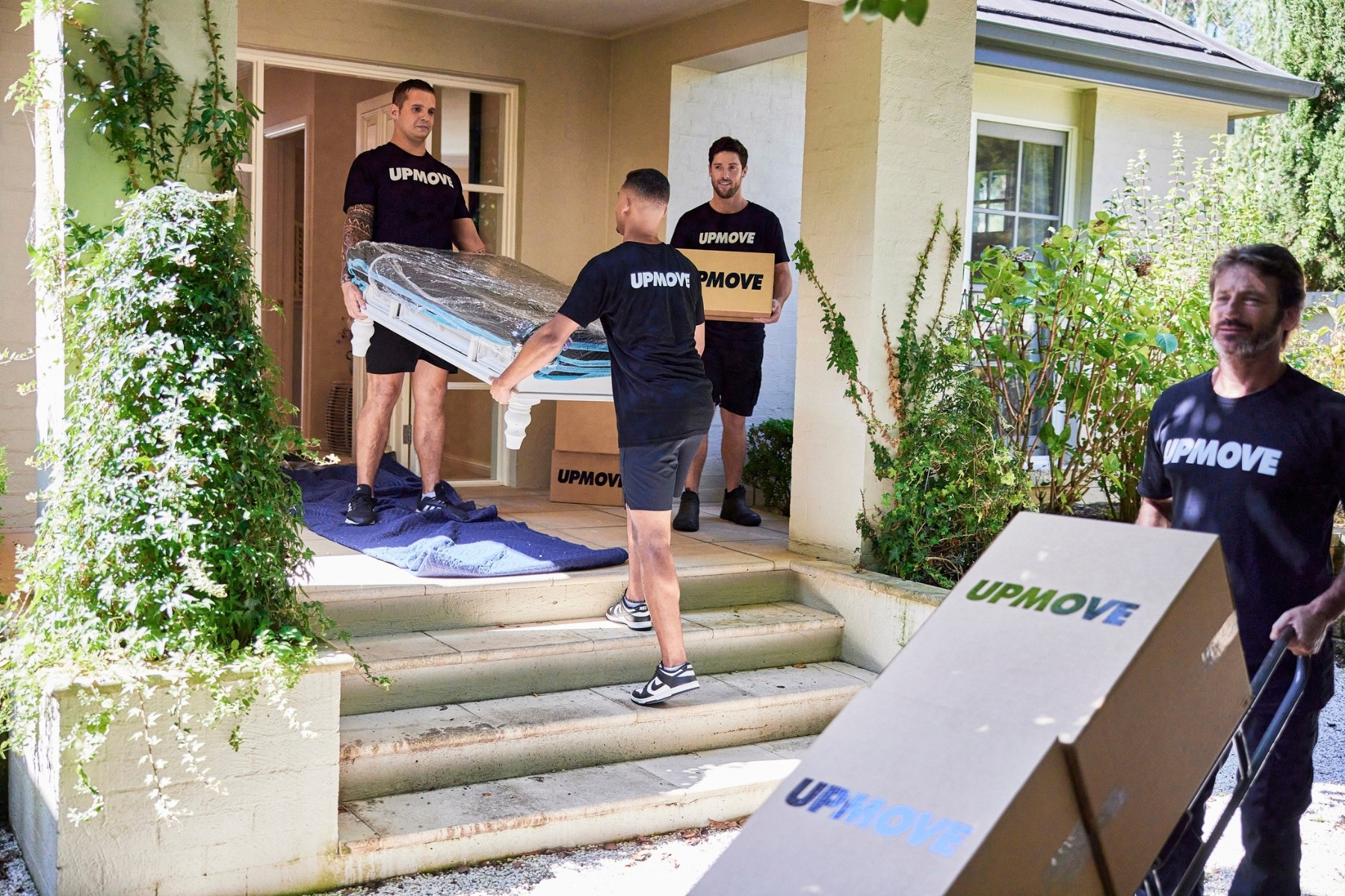 Upmove removalists carrying boxes and coffee table down porch stairs to truck
