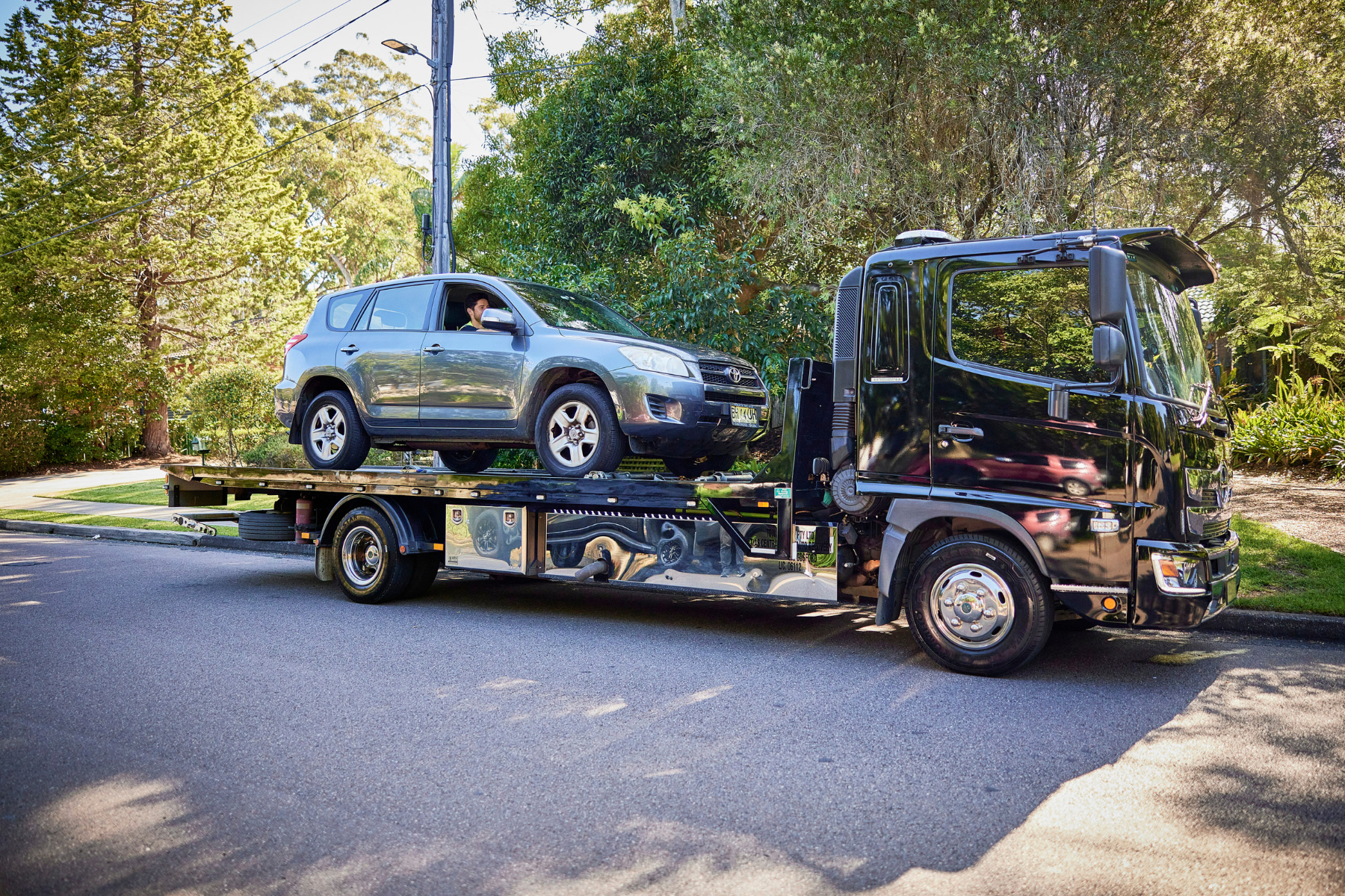 Car being transported on a flatbed truck in a suburban Australian street during an interstate move