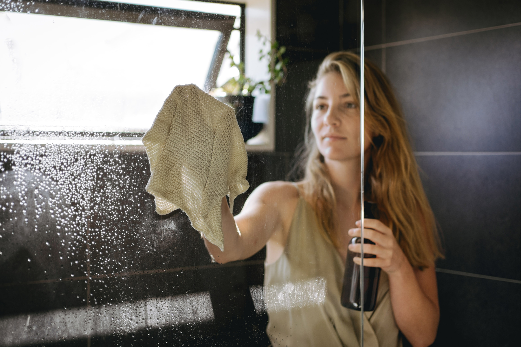 Woman cleaning bathroom mirror before unpacking in new home